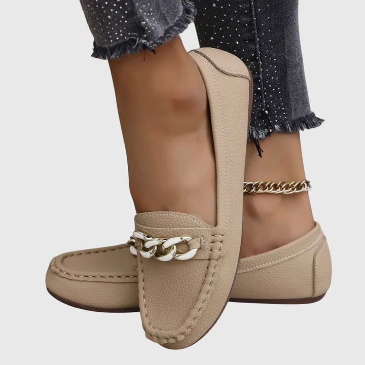 Kvinner som prøver slip-on loafers med kjededetalj. Viser stil, komfort og passform på foten.