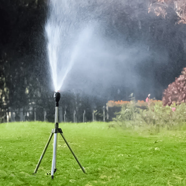 Hagesprinkler i aksjon, vanner frodig plen med justerbar spray fra stabilt stativ.