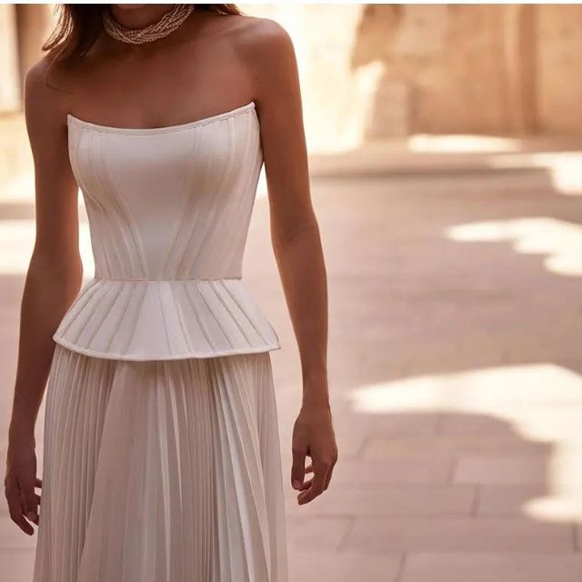 Nærbilde av plisseringene på den hvite off-shoulder gallakjolen. Viser elegant design og kvalitetsstoff.