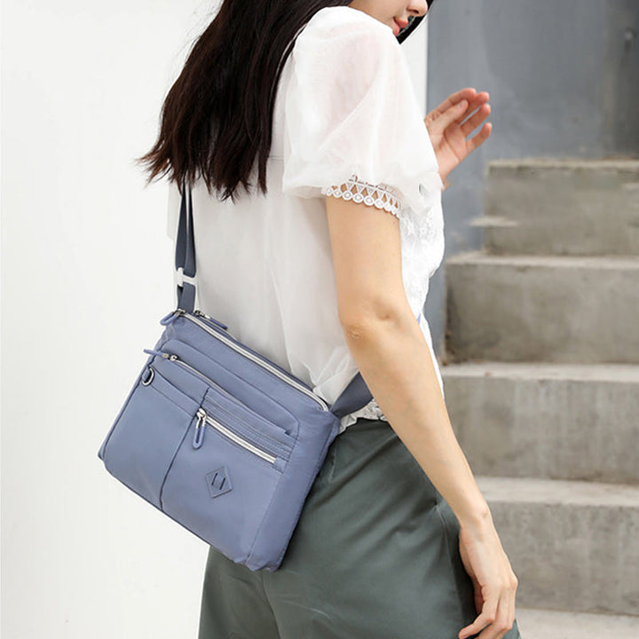 Lett crossbody-veske i nylon med glidelåslommer, ideell som reiseveske for kvinner.