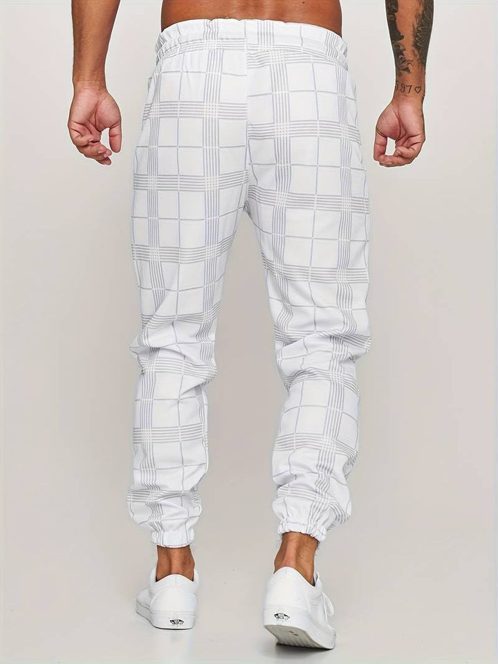 Ung mann i trendy herre rutete joggebukse, viser avslappet urban stil.