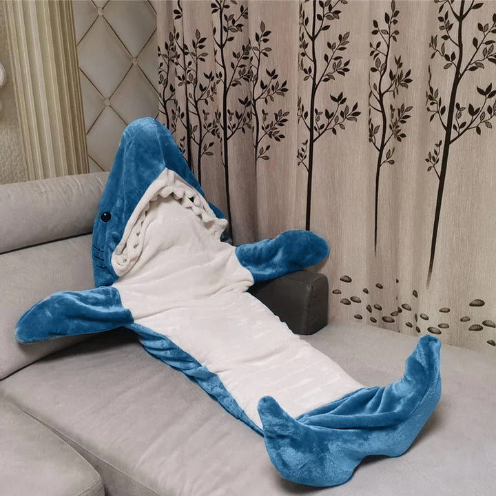Blå hai-onesie i myk fleece, sett fra siden. Viser detaljer som finner og hale. Varm hjemmeklær.