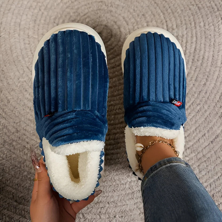 Par med beige unisex plysjtøfler med antiskli funksjon, sett fra siden for komfortabelt fottøy.