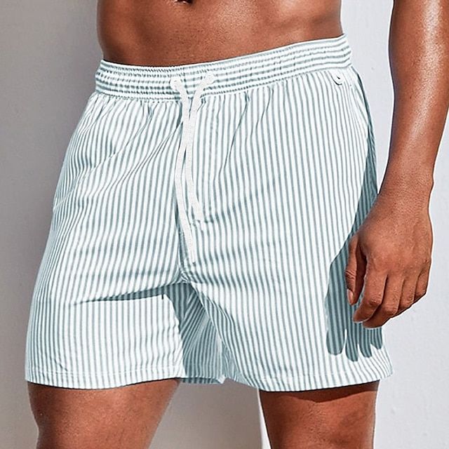 Mann går på stranden iført klassiske stripete badeshorts. Ideell for ferie og sommeraktiviteter.