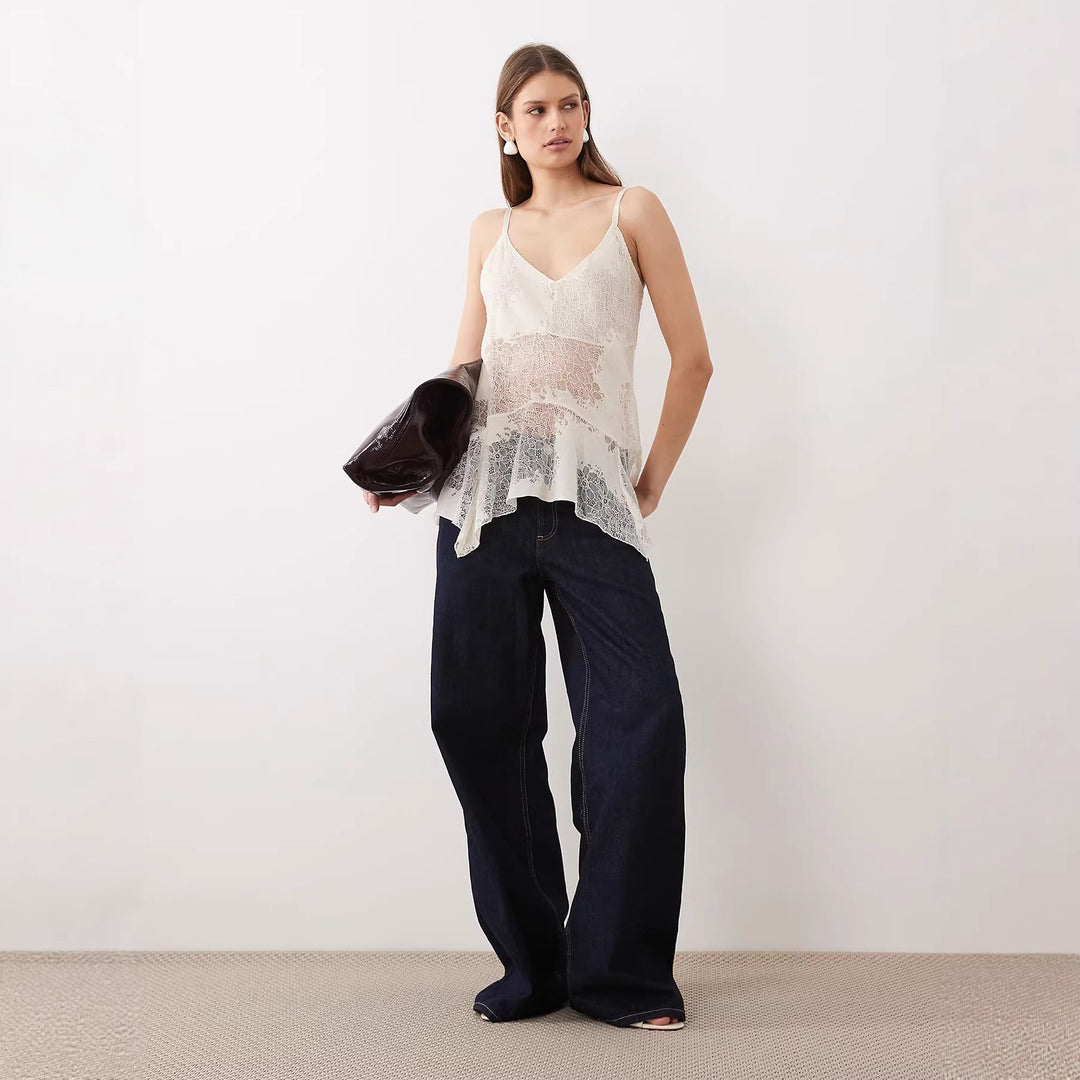 Asymmetrisk damebluse i blondestoff, hvit farge, ideell som festtopp. Elegant kvinnetopp med tynne stropper.