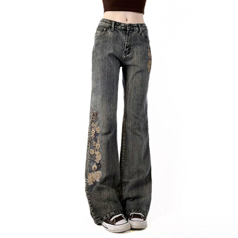 Trendy grå flared damejeans med delikat blomsterbroderi langs beina, perfekt for vår og sommer.