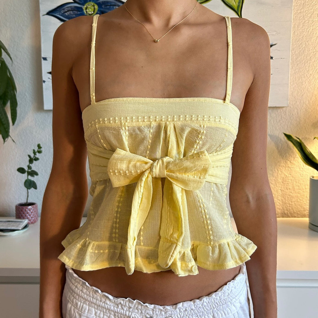 Gul sommertopp for dame med tynne stropper, elegante volanger og dekorative knapper.