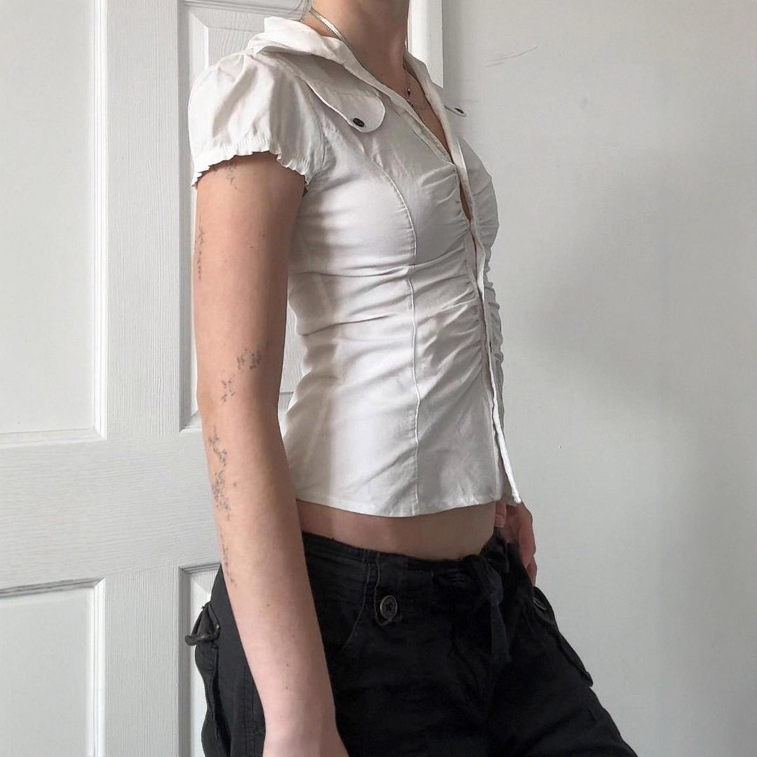 Hvit damebluse med elegante volanger og knappelukking. En figurnær festtopp for vår og sommer.