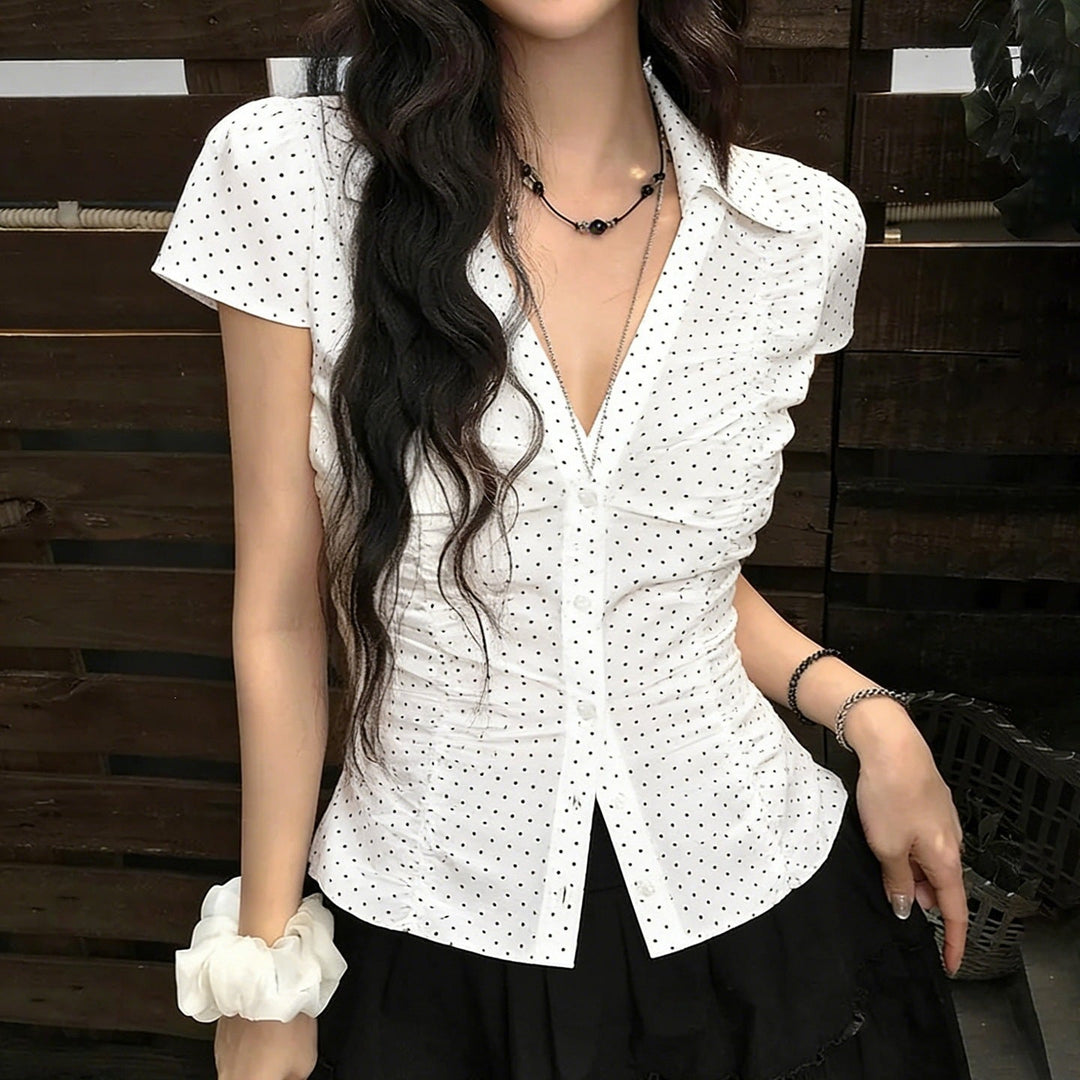 Elegant hvit damebluse med korte ermer, volanger og klassiske sorte prikker; perfekt sommerbluse og hverdagstopp.