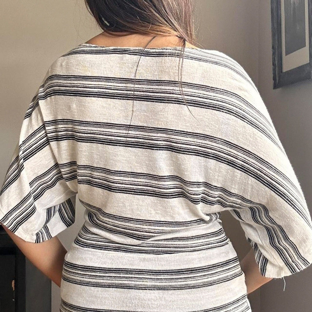 Nærbilde av grå oversized t-skjorte med detaljert blomster- og stripemønster på brystet, en vårtopp.