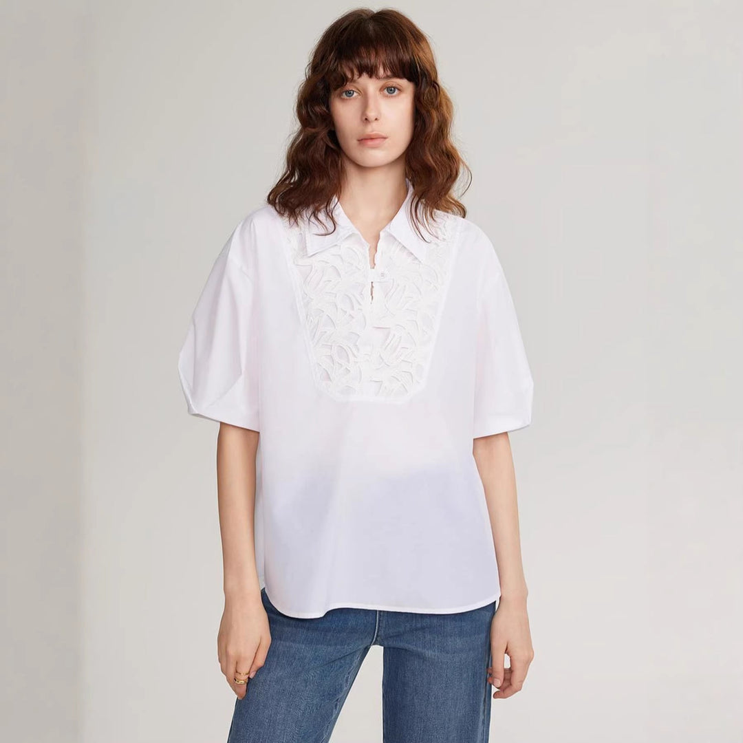 Nærbilde av detaljert broderi og delikate knapper på en elegant hvit damebluse.