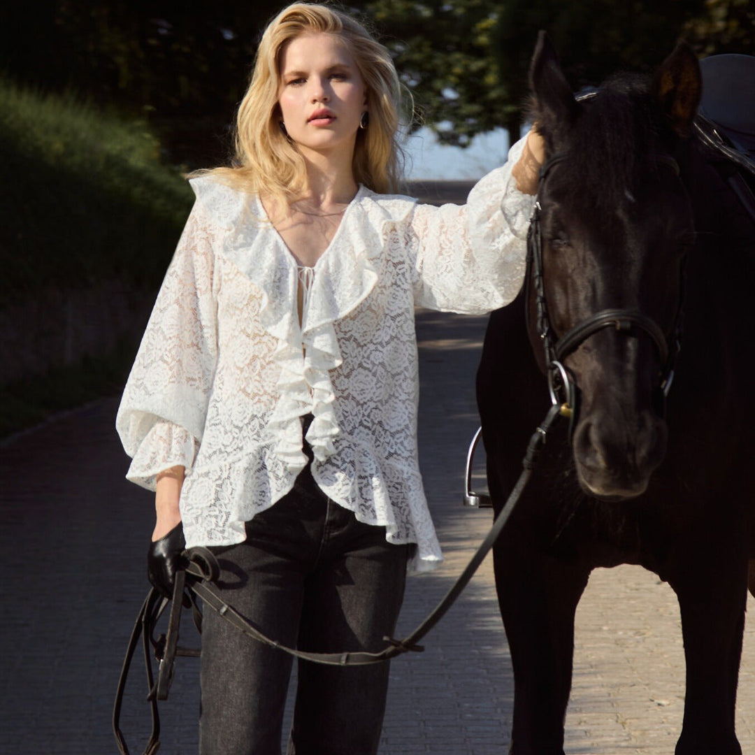 Modell iført trendy, hvit damebluse med elegante volanger. En flott vår- og sommer-topp for damegarderoben.