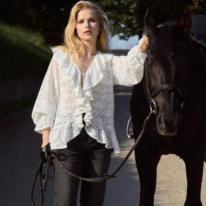 Modell iført trendy, hvit damebluse med elegante volanger. En flott vår- og sommer-topp for damegarderoben.