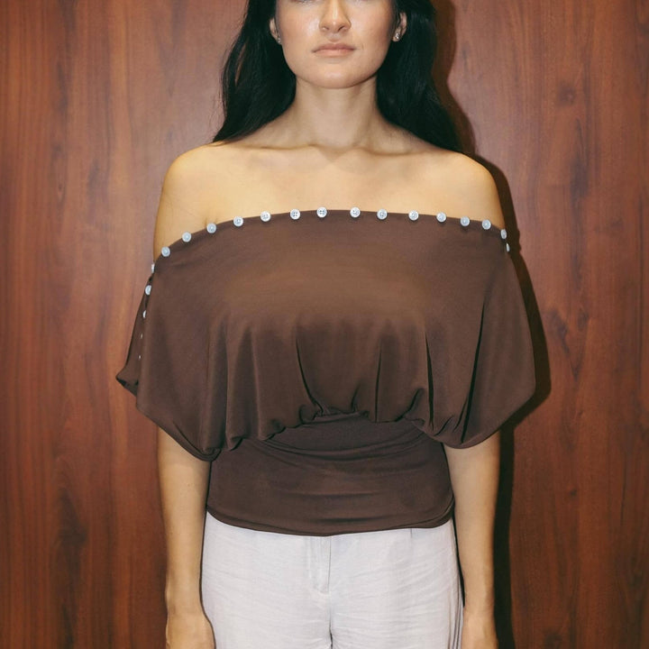 Nærbilde av elegant brun dame off-shoulder topp, viser delikate knapper og mykt stoff.