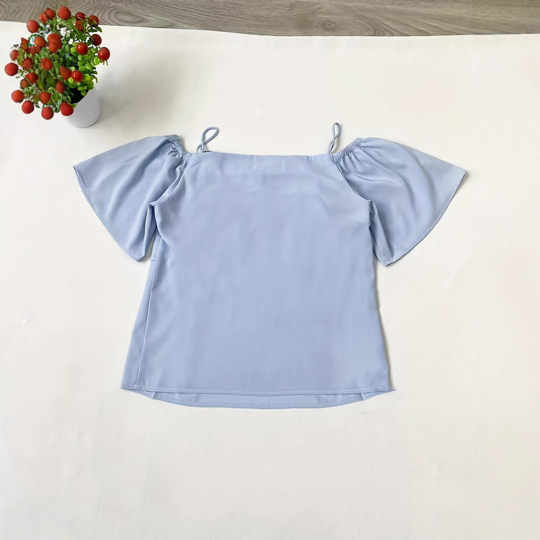 Modell iført elegant himmelblå damebluse med volanger og åpen skulder for en trendy sommerlook.