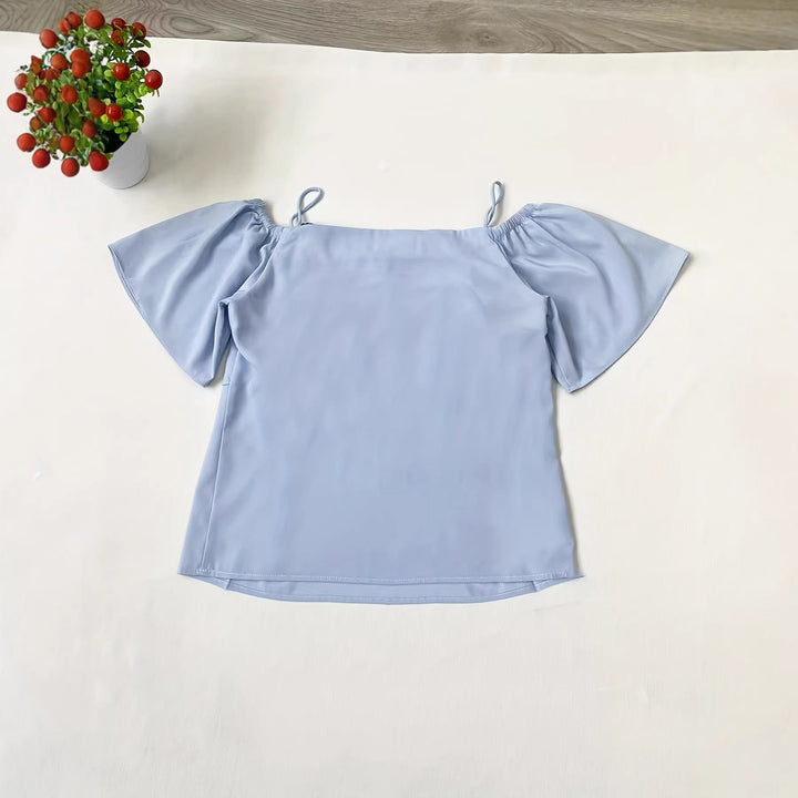 Modell iført elegant himmelblå damebluse med volanger og åpen skulder for en trendy sommerlook.