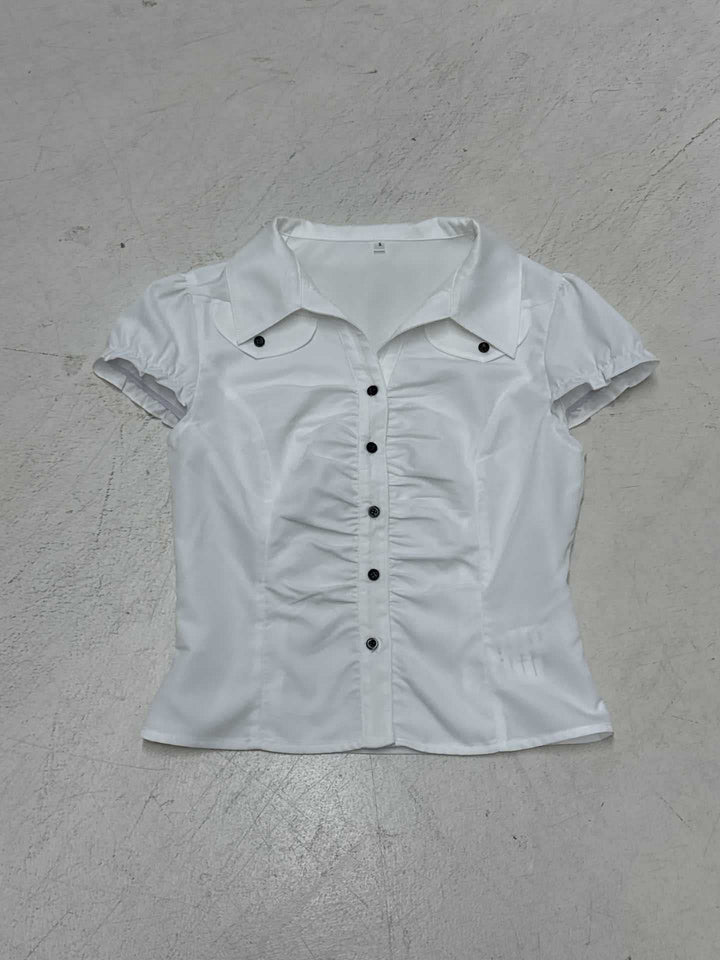 Detaljebilde av figurnær damebluse som viser elegante volanger og den diskrete knappelukkingen.