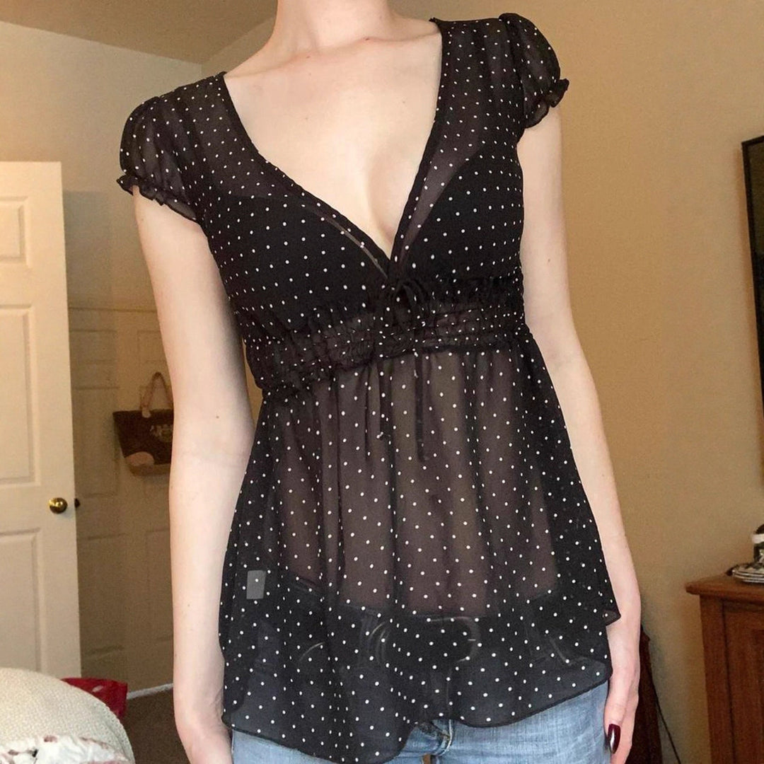 Damebluse med volanger sett fra siden på modell, fremhever lett stoff og lekent polkaprikket design.