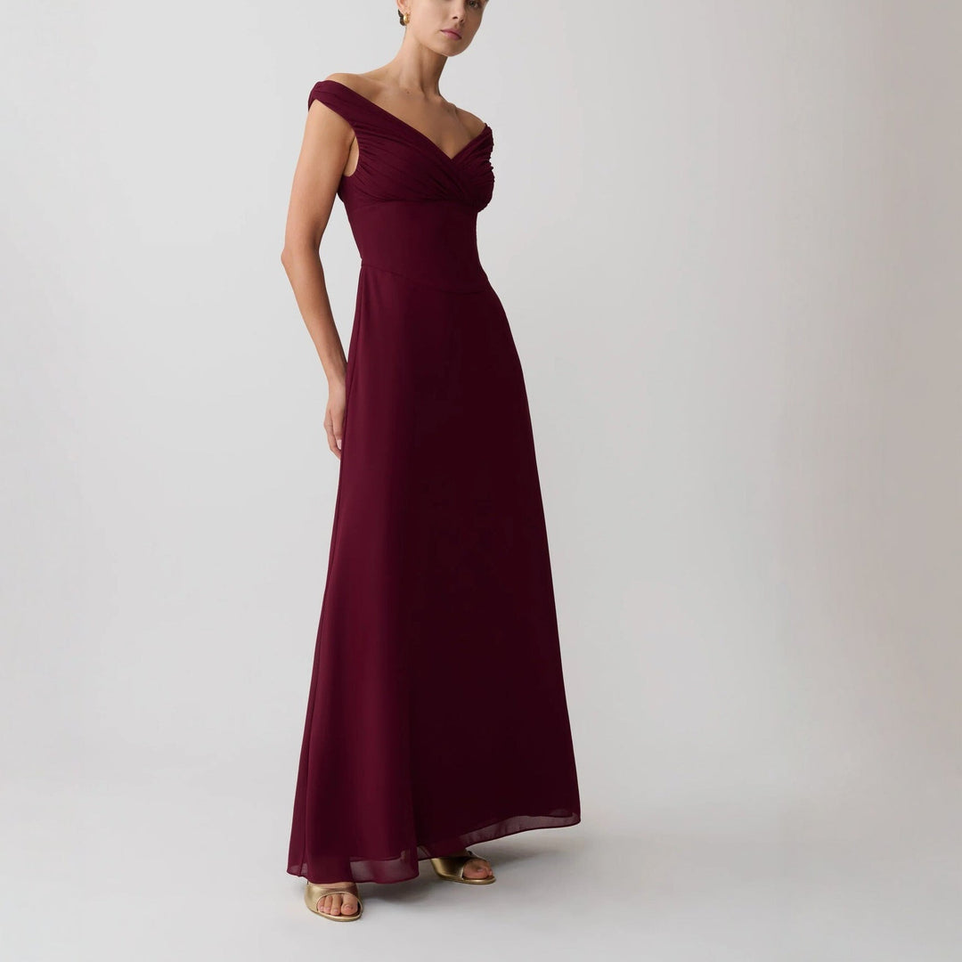 Stilfull festkjole i bordeauxrød med elegant skulderfri design og myk drapering, et glamorøst kveldsantrekk.