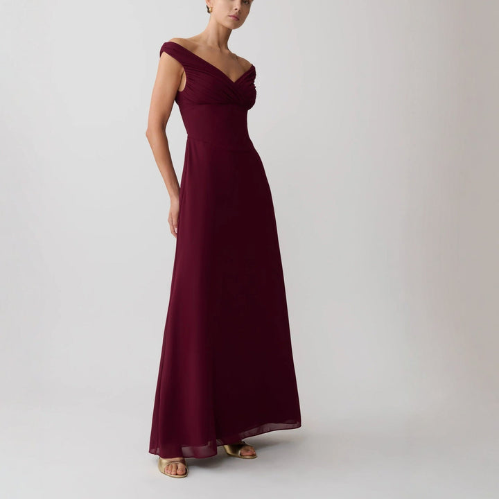 Stilfull festkjole i bordeauxrød med elegant skulderfri design og myk drapering, et glamorøst kveldsantrekk.