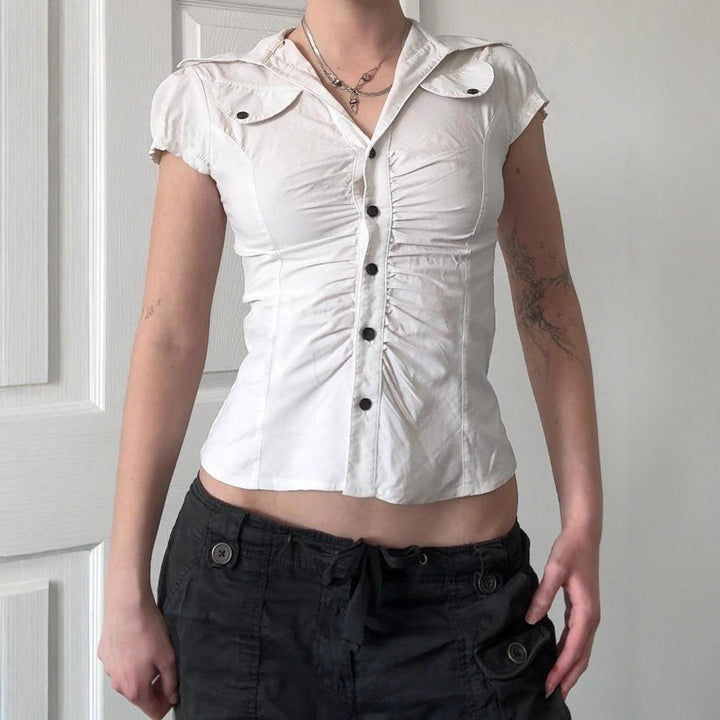 Elegant hvit figurnær damebluse med volanger og diskret knappelukking, perfekt for vår og sommer.