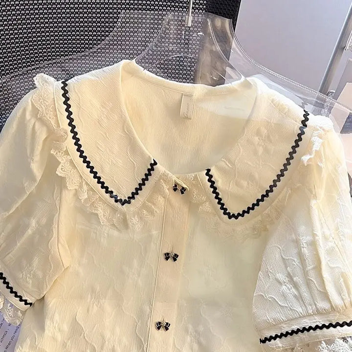 Elegant aprikos damebluse med Peter Pan-krage og feminine puffermer, perfekt for sommer og fest.