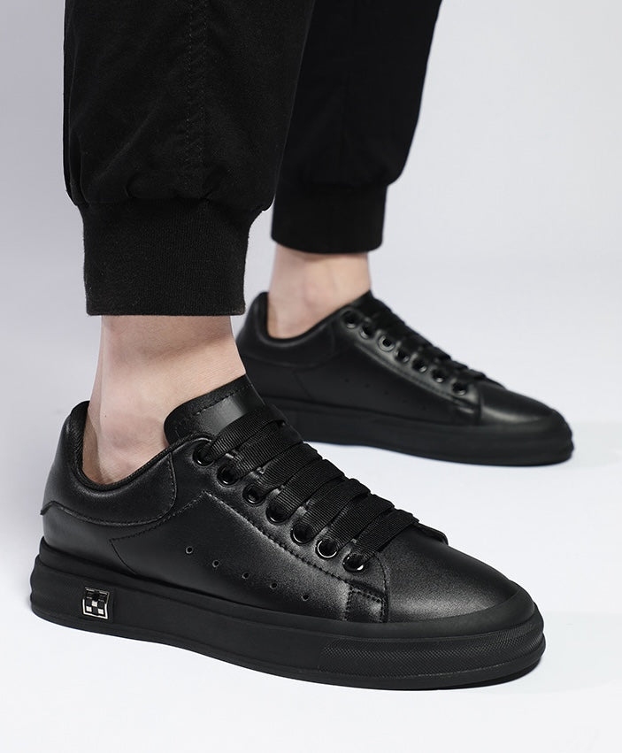 Herremodell bærer stilige svarte og hvite høydeøkende sneakers med 6 cm skjult hæl.