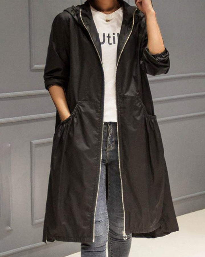 Dame lang trenchcoat med hette sett bakfra, stilrent yttertøy perfekt for urbant miljø og regn.