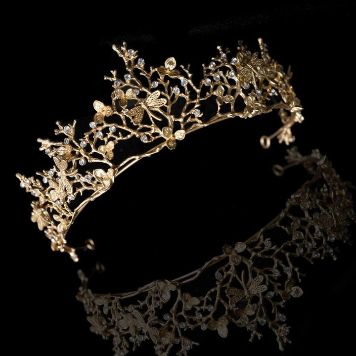 Nærbilde av øyenstikkerdetaljer på en barokk gulltiara med intrikate mønstre og rhinestones.