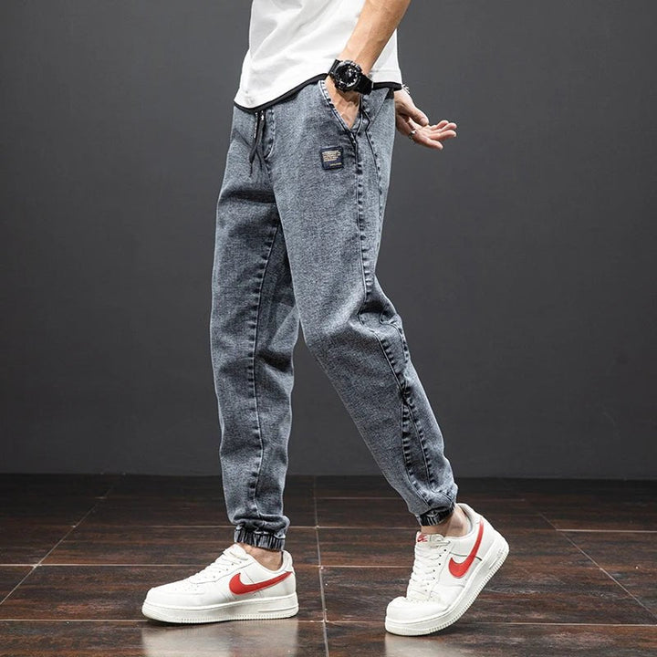 Bakside av herres denim joggere med praktiske lommer og elastiske ankler, perfekt for komfort.