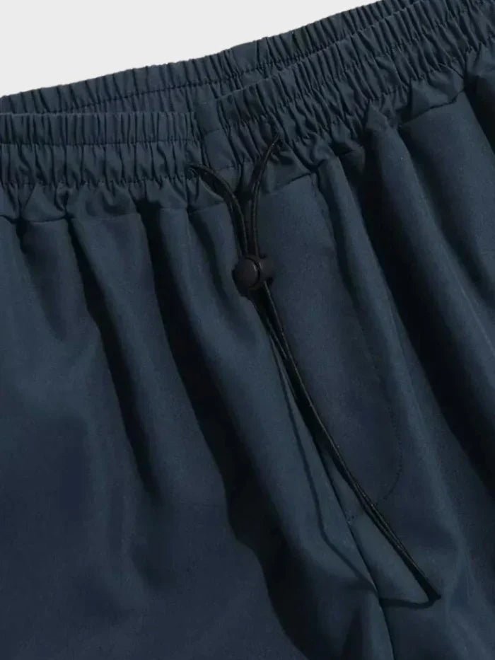 Helbilde av menns streetwear cargo-bukser i sort, med løs passform og justerbar linning. Ideell for urban stil.
