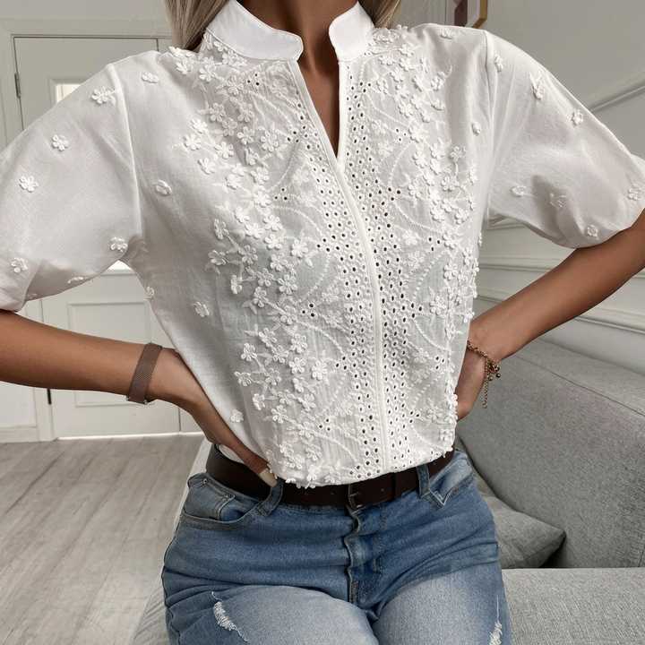 Feminin kvinnebluse, hvit, med intrikat blomsterdesign og stilig ståkrage. Perfekt for ulike anledninger.
