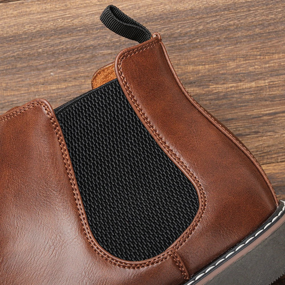 Detaljbilde av skinntekstur på svarte Chelsea-støvler for menn. Elegant og holdbart materiale.